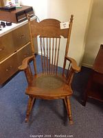 Full view of the wooden rocking chair showing the press back, armrests, carved details on the backrest, turned legs and rocking base