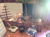 Photo showing a variety of decorative items including a brass planter with a silk tree, vintage pink and white vase, blue and white ceramic vase, and several other ceramic planters and pots.
