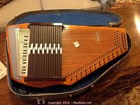 Whole view of vintage wooden autoharp by Oscar Schmidt in open hard case with blue padded interior, showing strings and chord bars.