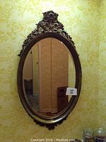 Oval decorative mirror with dark carved frame hanging on yellow floral wallpapered wall