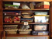 Wooden cabinet shelves filled with plastic containers and boxes of craft supplies including wooden spools and ribbons.
