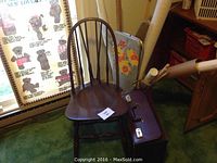 Wooden chair with spindled backrest, a brown carrying case on the floor in front, and rolled fabrics and a floral patterned bag stored in a basket beside the chair.