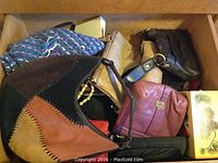 Drawer with multiple purses in different styles and colors including patchwork leather and tan leather purse, maroon purse, black handbag, and a decorative box.