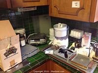 Overview of lot items on kitchen counter including boxed popcorn popper, food scale, waffle maker, ice cream maker, inversion blender, herb mill, and citrus juicer.