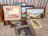 Photo showing eight varying framed art pieces arranged on the floor against a striped wallpaper background including landscapes, portraits, and nature subjects.