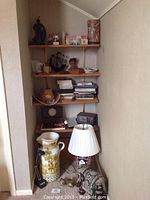 Overall view of corner shelves with various decor items including the lamp, elephant statue, large pitcher, and wooden birds on floor.
