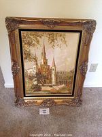 Clear photo of framed cathedral artwork showing ornate gold frame and cathedral with three spires.