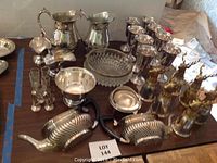 Overview of silver plate goblets, pitchers, bowls, wall pitchers with deer heads, and glass serving pieces on table.