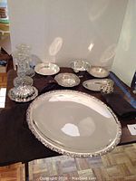 Full view of silver platter with decorative edge, several small silver bowls, and pair of crystal glass candlesticks on a table.