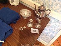 Full lot on wooden table showing teapot, two candlesticks, baby rattle ring, and pierced bowl.
