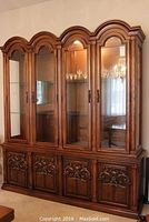 Front view of the china cabinet showing four glass doors on top and four solid carved wood doors below with brass pulls.