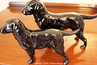Both black ceramic dog figurines shown on wood surface, capturing size and finish.