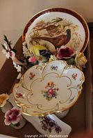 Porcelain bird figurines including finch and European goldfinch on branch with flowers arranged in box