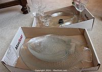 Large clear glass fish-shaped platter and smaller plates shown in cardboard boxes