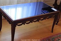 Full view of wooden coffee table with reflective blue glass top and carved detailing