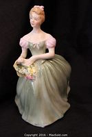 Front view of Royal Doulton porcelain figurine of woman wearing green dress with pink sleeves holding basket of flowers.