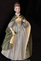 Front view of the figurine showing the lady in a light blue dress with a green cape and floral patterns.