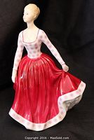 Front angled view of the Royal Doulton figurine depicting a woman in a patterned top and red skirt holding the skirt edge.