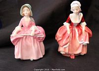 Front view of two Royal Doulton figurines Goody Two Shoes and Bo-Peep placed side by side on black background.