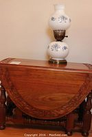 Mahogany gate leg table closed with carved edges and turned legs, small lamp on top