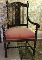 Front view of the antique wooden open armchair showing carved wood detailing and pink upholstered seat.