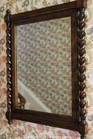 Full view of rectangular mirror with dark stained wood frame and twist side supports hung on floral wallpaper