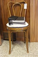 Wooden bentwood style chair with seat cushion, showing wear and holding stacked books and folder.