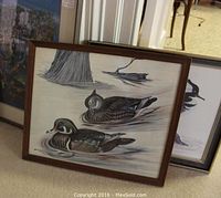 Framed original acrylic painting and prints leaning against wall, showing two wood ducks on water with driftwood and tree.