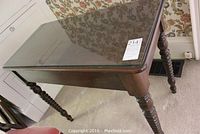 View of the wooden table with glass top showing turned legs and glass surface reflecting surrounding decor.