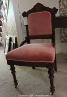 Front angled view showing pink upholstered seat and backrest, dark wood frame, and turned front legs with casters.