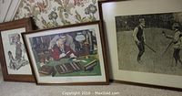 Three framed prints displayed on carpet with wallpaper background, showing two smaller colorful Norman Rockwell prints and one larger black and white A.B. Frost print.