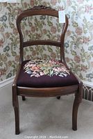 Front view of balloon back needlepoint chair showing floral needlepoint seat and wood frame with light wear.