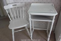 Vintage white phone table and painted wood chair set against wallpaper.