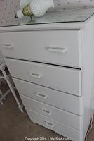 View of the white five drawer dresser showing the front and glass protective top with lamp placed on top.