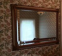 Rectangular mirror with carved wooden frame in floral wallpapered room
