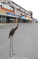 Full-height front view of the heron sculpture standing on pavement outside a storefront