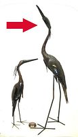 Front view of two heron sculptures, large 42in steel heron indicated by red arrow alongside smaller heron and roll of quarters for scale.