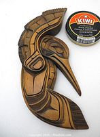 Close-up image of the hand-carved hummingbird sculpture placed beside a small can of Kiwi black shoe polish for scale, showing intricate carving details and wood texture.