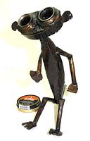 Front view of small metal monkey sculpture alongside a Kiwi shoe polish tin for scale.