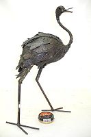 Full side view of the recycled steel ostrich sculpture standing with legs outstretched next to a small tin for size reference.