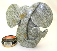 Front view of polished green-grey serpentine stone elephant sculpture with natural brown streaks, includes shoe polish can for scale