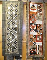 Two handwoven and painted textile pieces hanging vertically against a wall. Left textile features geometric star patterns with cement background. Right textile with various traditional African painted motifs in rust, black, white and cement colors.