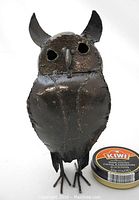 Front view of the recycled steel owl sculpture beside a can of Kiwi shoe polish for size reference; owl is black with visible welds and hollow eyes.