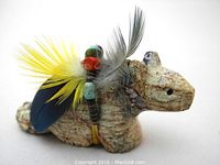 Front view close-up of the carved stone beaver fetish showing the face, feather, and bead decorations.