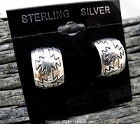 Close-up photo of a pair of sterling silver stud hoop earrings with Navajo rain cloud and lightning bolt engravings on a black HOLDER labeled 'STERLING SILVER'. The earrings have a polished finish and display traditional Native American design elements.