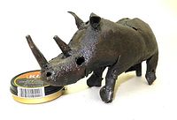 Front-left angled view of recycled steel rhino sculpture with a tin can for scale. Shows two large horns, eyes as holes, short ears, textured metal surface and four legs.