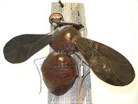 Front view of large bumble bee metal sculpture mounted on wooden plank showing detailed wings and body segments.