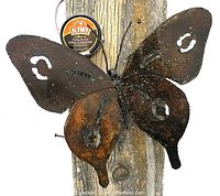 Close-up image showing the large metal butterfly mounted on a wood surface with visible rust texture and cut-out wing details. Kiwi shoe polish tin nearby for scale.