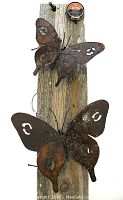 Two shots of a small steel butterfly sculpture welded by Innocent Luwagala, mounted on a rustic wood plank.