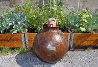 Front view of spherical steel pot with open neck, surrounded by planter boxes